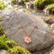 Rose gold paw pendant necklace displayed on a creek-side stone