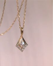 Close-up of a gold geometric pendant necklace with a kite-shaped clear gemstone and sparkling halo stones