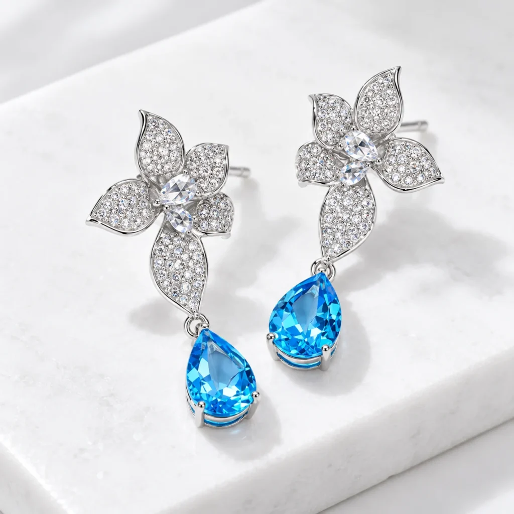 45-degree view of Azure Blossom earrings showing sculpted silver petals and blue topaz drop settings