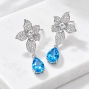 45-degree view of Azure Blossom earrings showing sculpted silver petals and blue topaz drop settings
