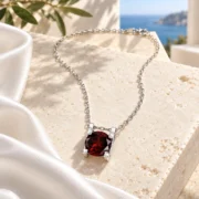 Angled view of the Ember Glow necklace showing its round wine-red garnet and silver prongs