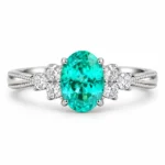 Front view of a teal cluster ring with an oval blue-green center and clear side stones