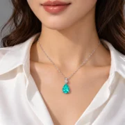 styled.webp Blue-green teardrop pendant displayed against a warm golden background